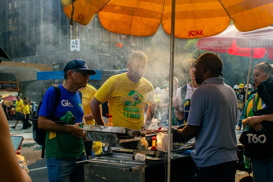 Vendedores de rua assando carne sob guarda-sol laranja