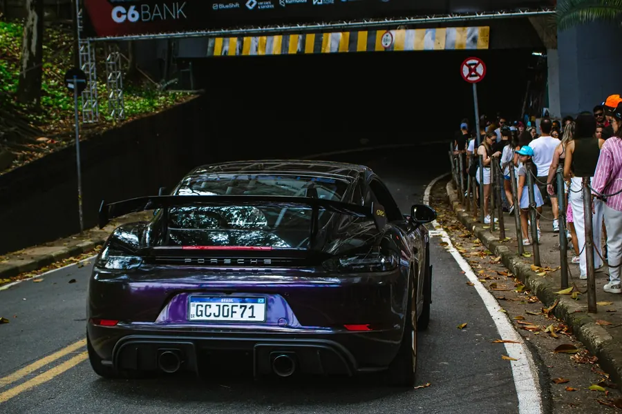 Porsche roxo de traseira saindo do túnel, com público na calçada