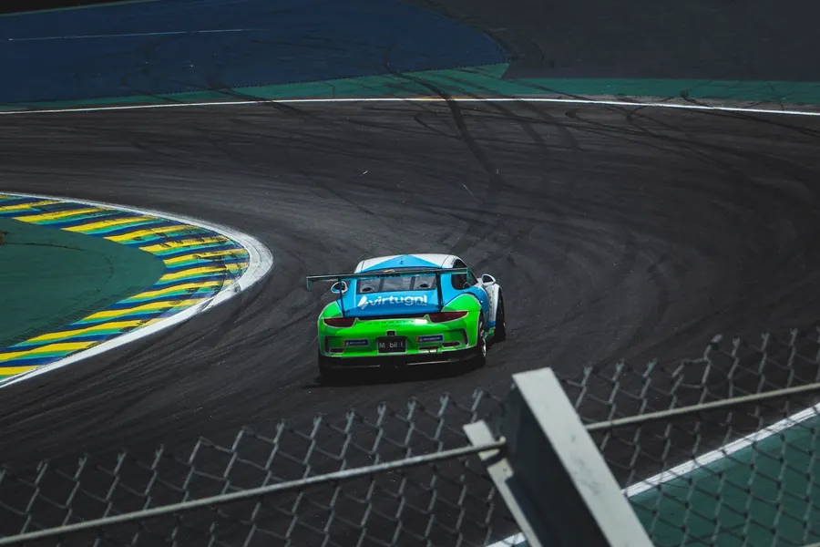 Porsche verde e azul contornando a curva sobre a zebra